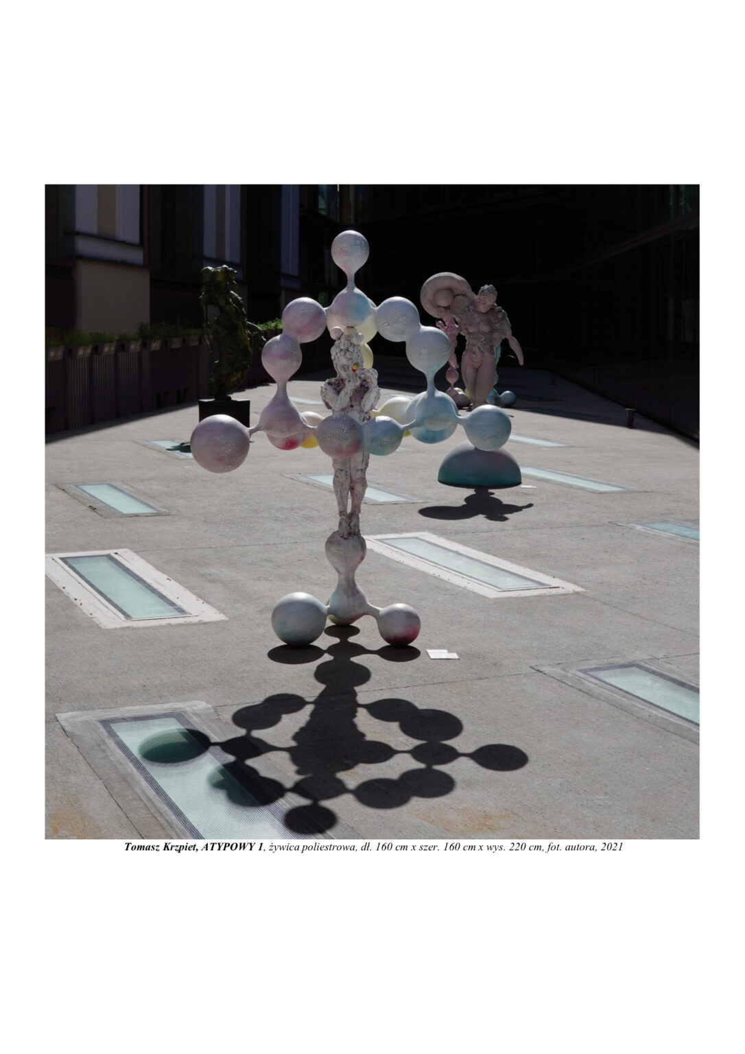 Rzeźba chłopca zbudowanego z atomów, który stoi na kulistym molekule i otoczony jest również molekułami. Kompozycja rzeźbiarska w kolorystyce barw podstawowych (żółtym, czerwonym i niebieskim)